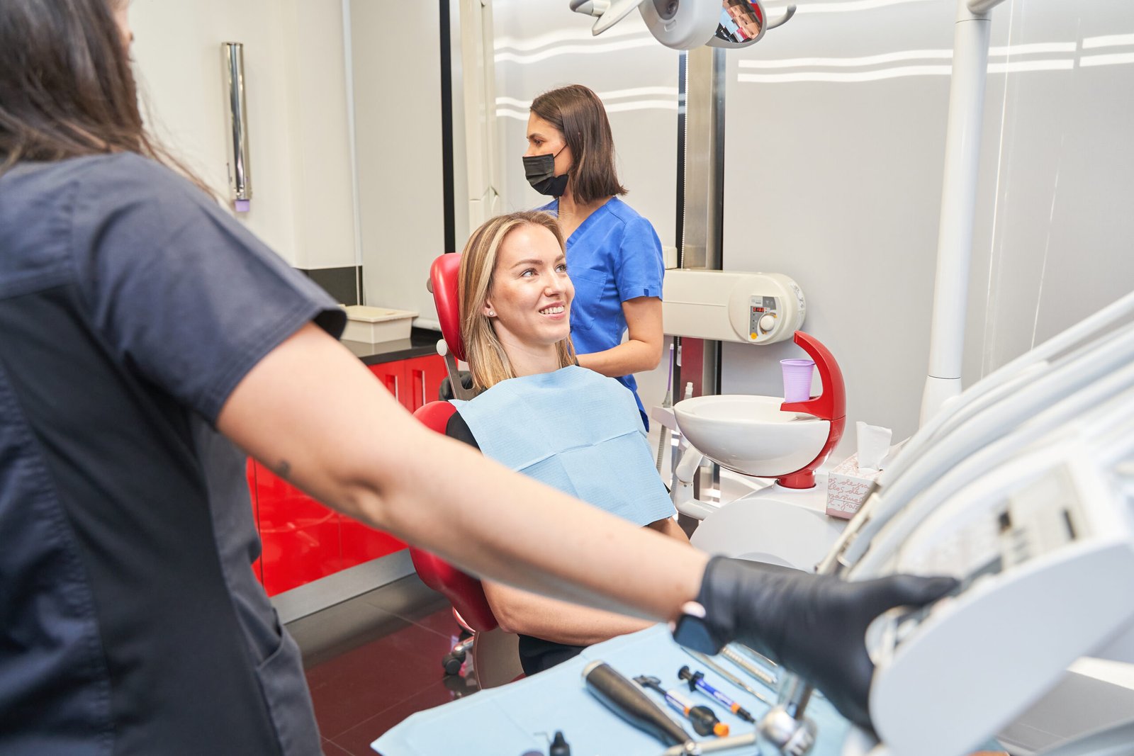 dentist with face mask talking to blonde woman during dental procedure at dental clinic.