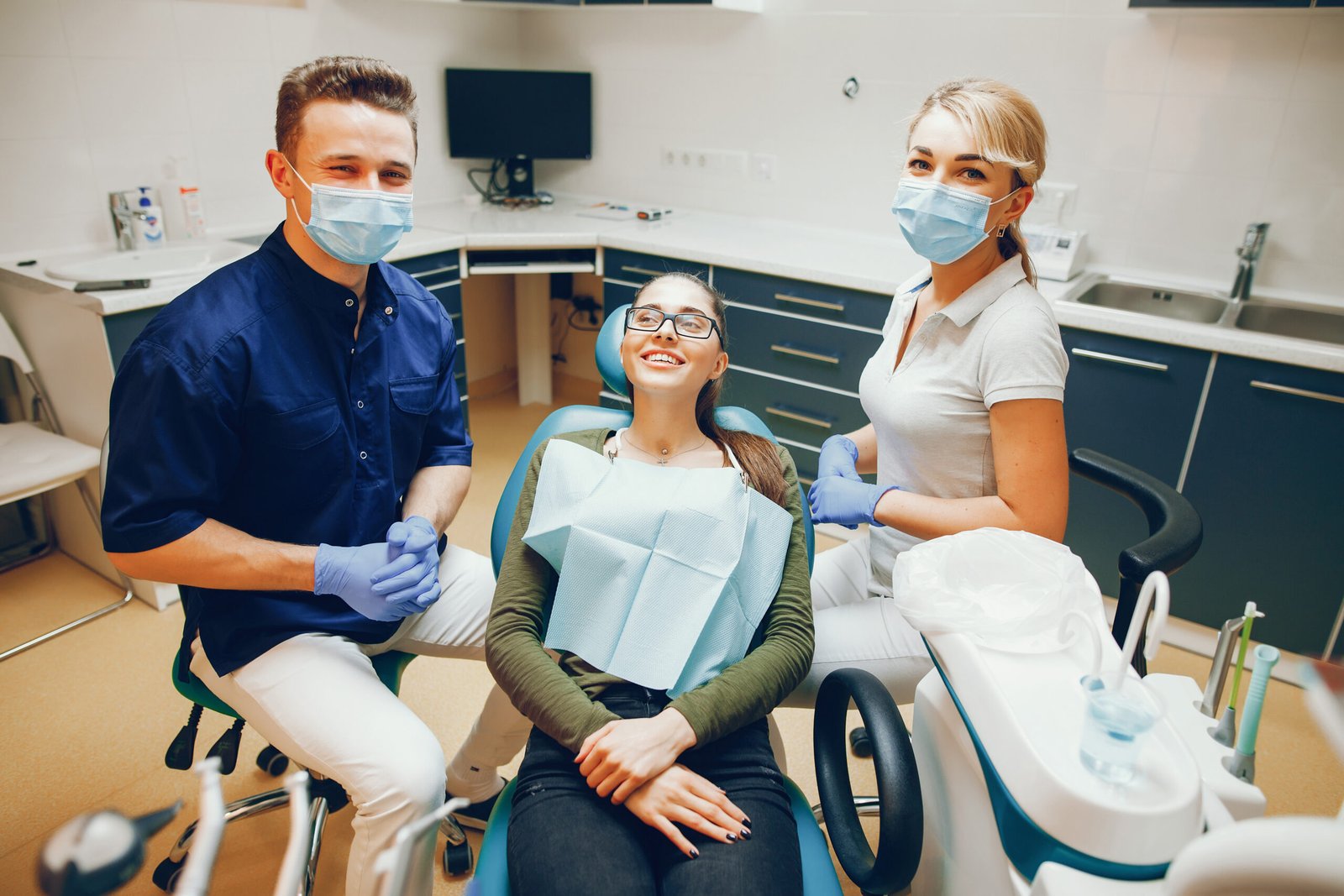 A young and beautiful girl treats her teeth with a dentist and assistant helps him