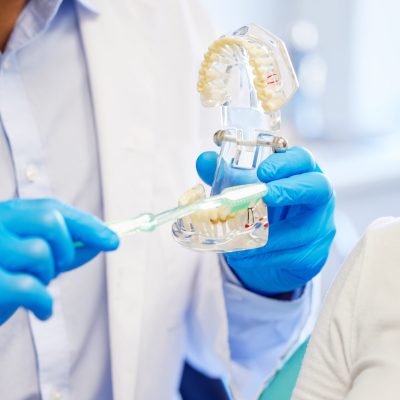 Shot of a dentist showing his patient a model of teeth before her procedure.